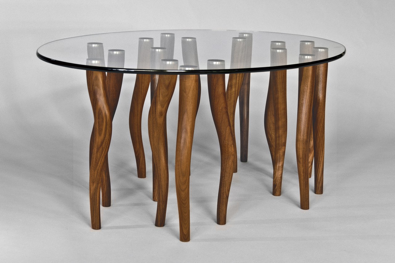 Oval glass coffee table with wood and stainless steel legs carved by Seth Rolland custom furniture